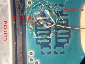 Closeup a thin copper wire soldered to a pad in between camera and flash on the a5xelte. The pads are in a horizontal 2x6 grid. The top left is probably Rx, the one below is Tx